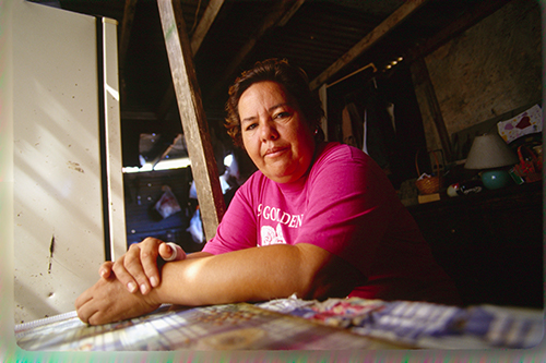 Hispanic woman sitting at a table inside her Colonia home.