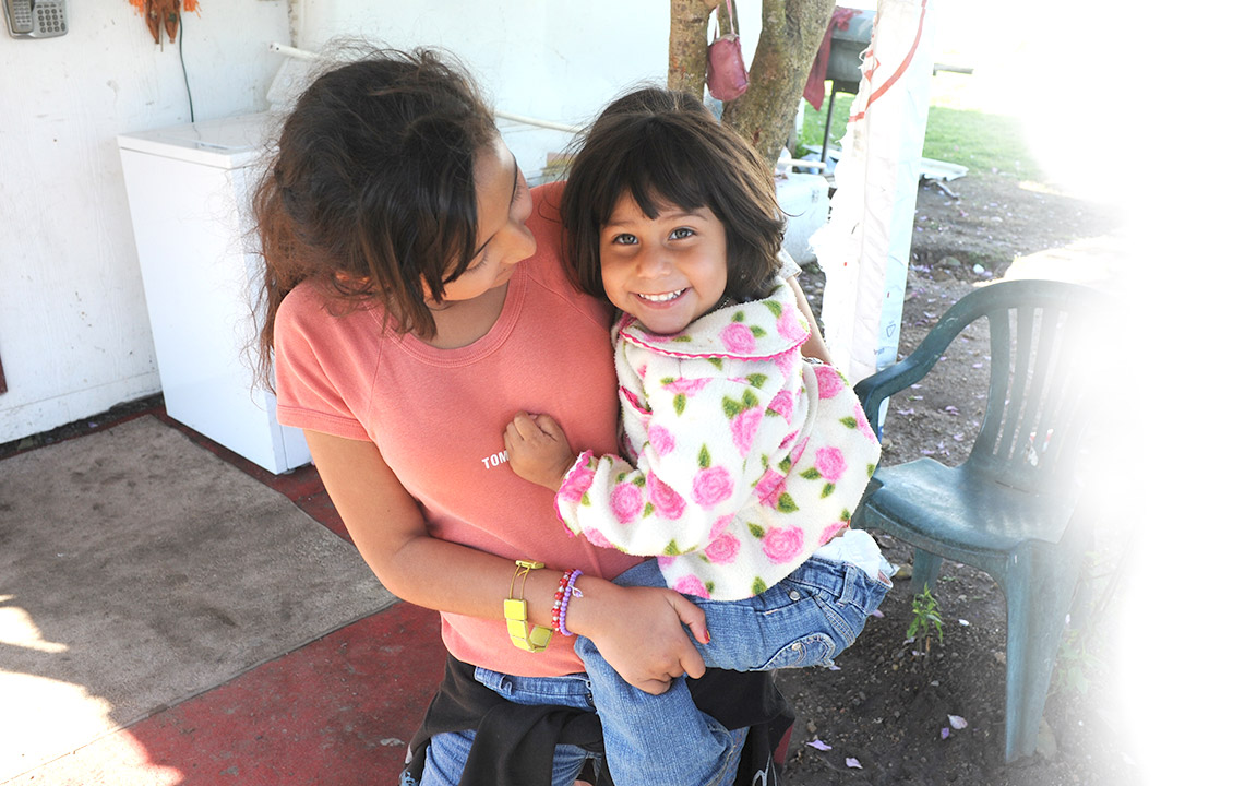 A young girl from the colonias holding her baby sister.