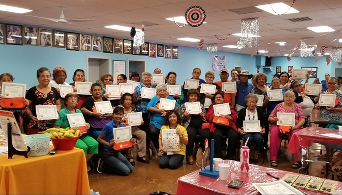 A Promotora posing with a class of community members holding up certificates.